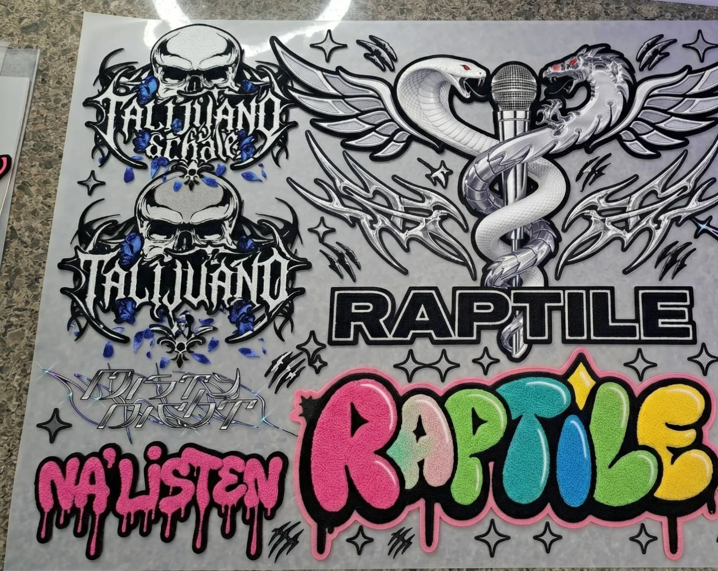 Printed heat-transfer sheet with Talijuano skull marks, the Raptile caduceus, a bubble Raptile wordmark and a pink drip Na'Listen script